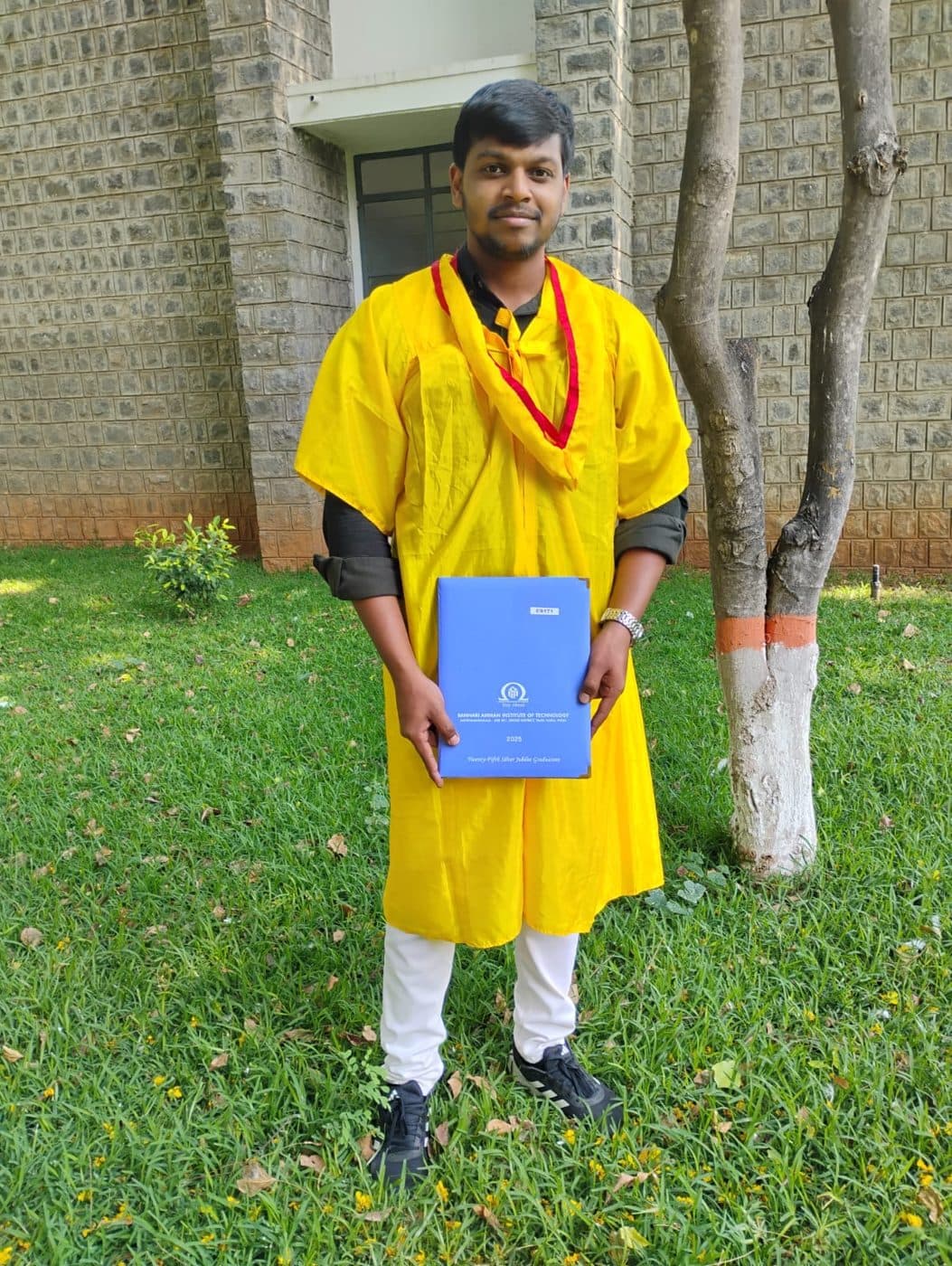 Harish in a graduation gown holding a folder.